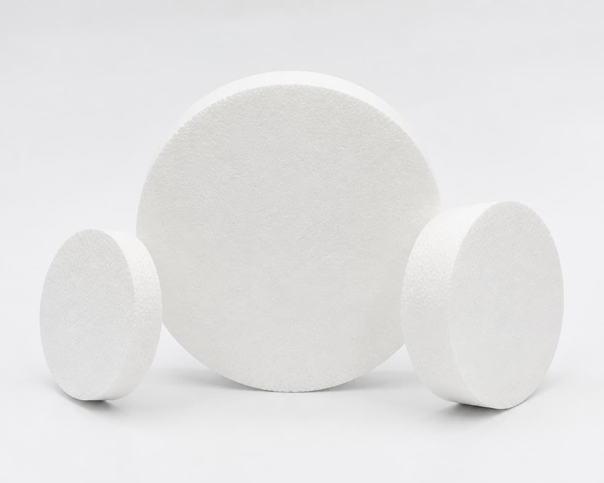Trois disques ronds blancs en polystyrène de diamètres différents posés sur un fond neutre lumineux, l'un incliné pour montrer son épaisseur.