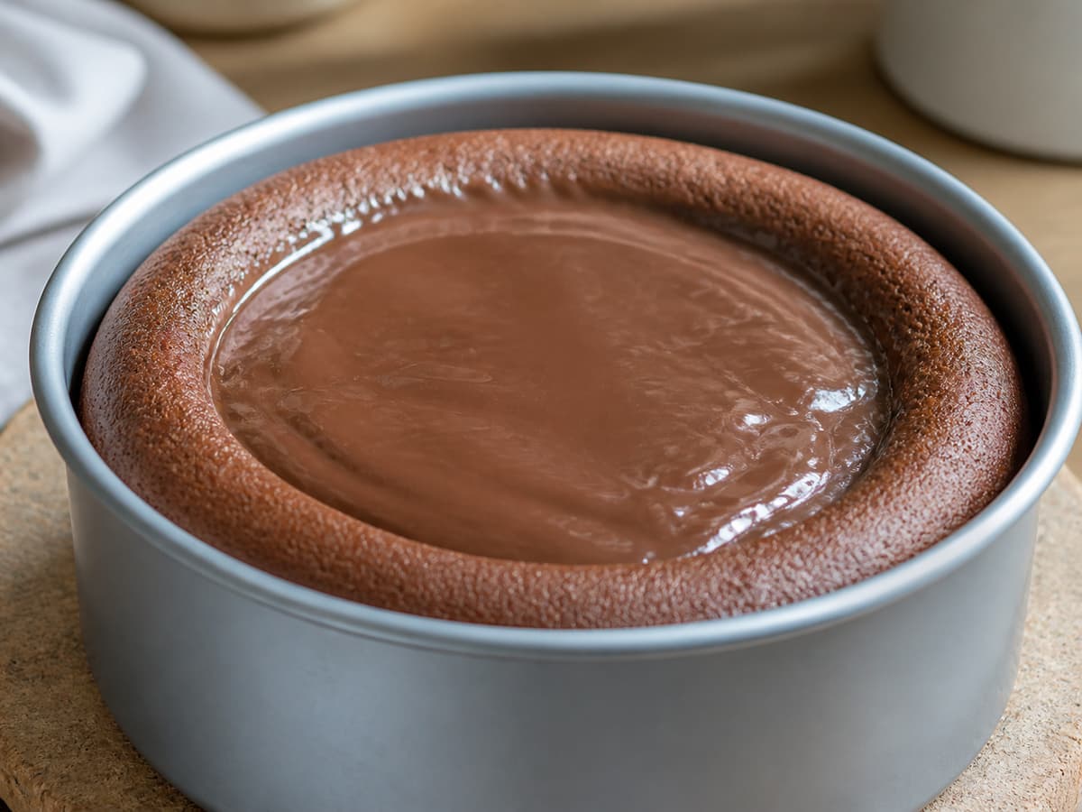 Flan au chocolat dans un moule rond posé sur une surface, avec des bords cuits et gonflés et un centre brillant encore souple.