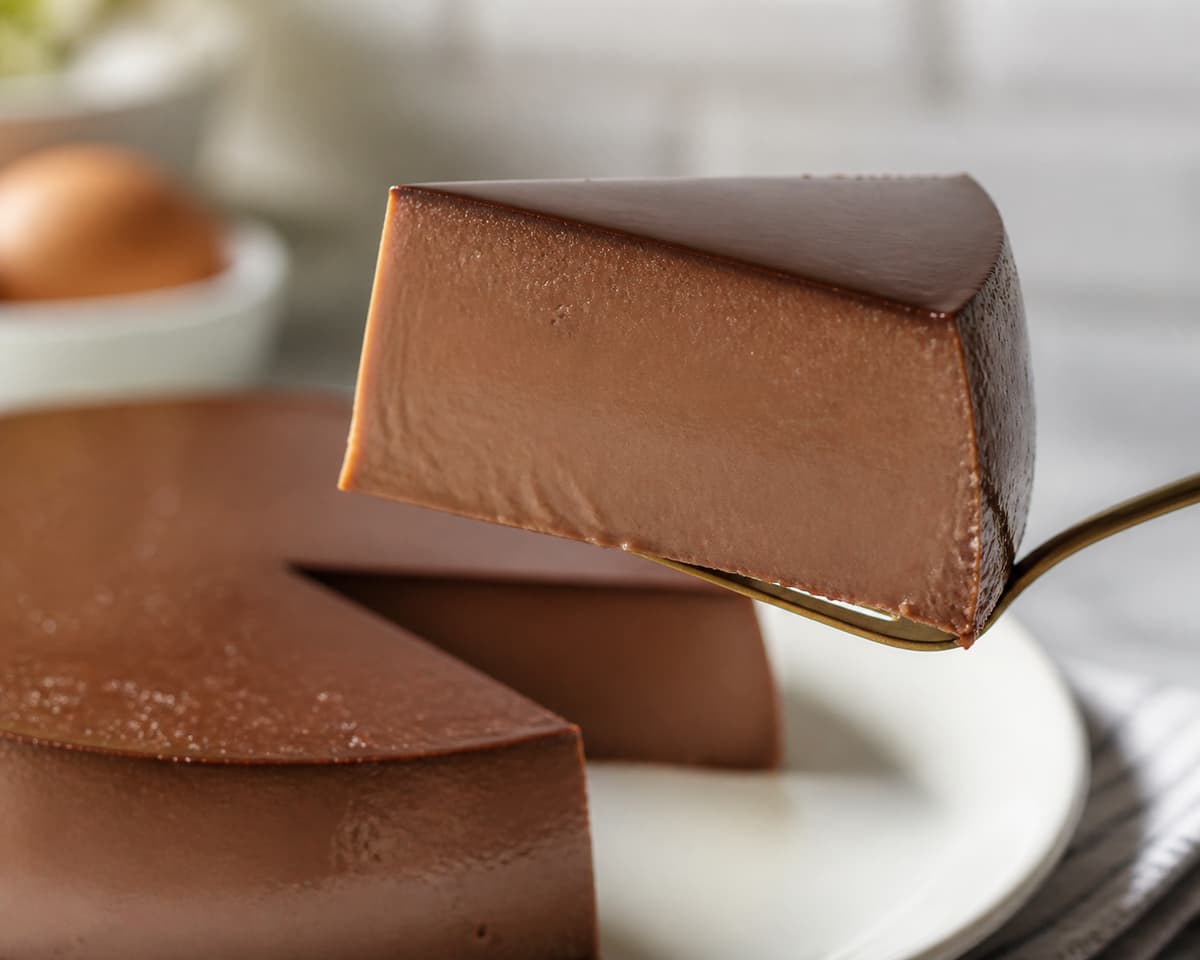Part de flan au chocolat bien froide, soulevée par une fourchette, montrant une coupe lisse, droite et une texture dense et crémeuse.