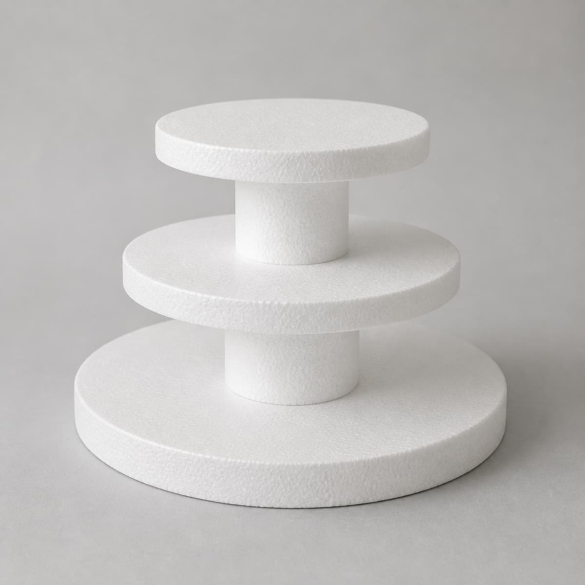 Support de pièce montée en polystyrène blanc à trois niveaux circulaires superposés, photographié de trois quarts sur une surface plane.