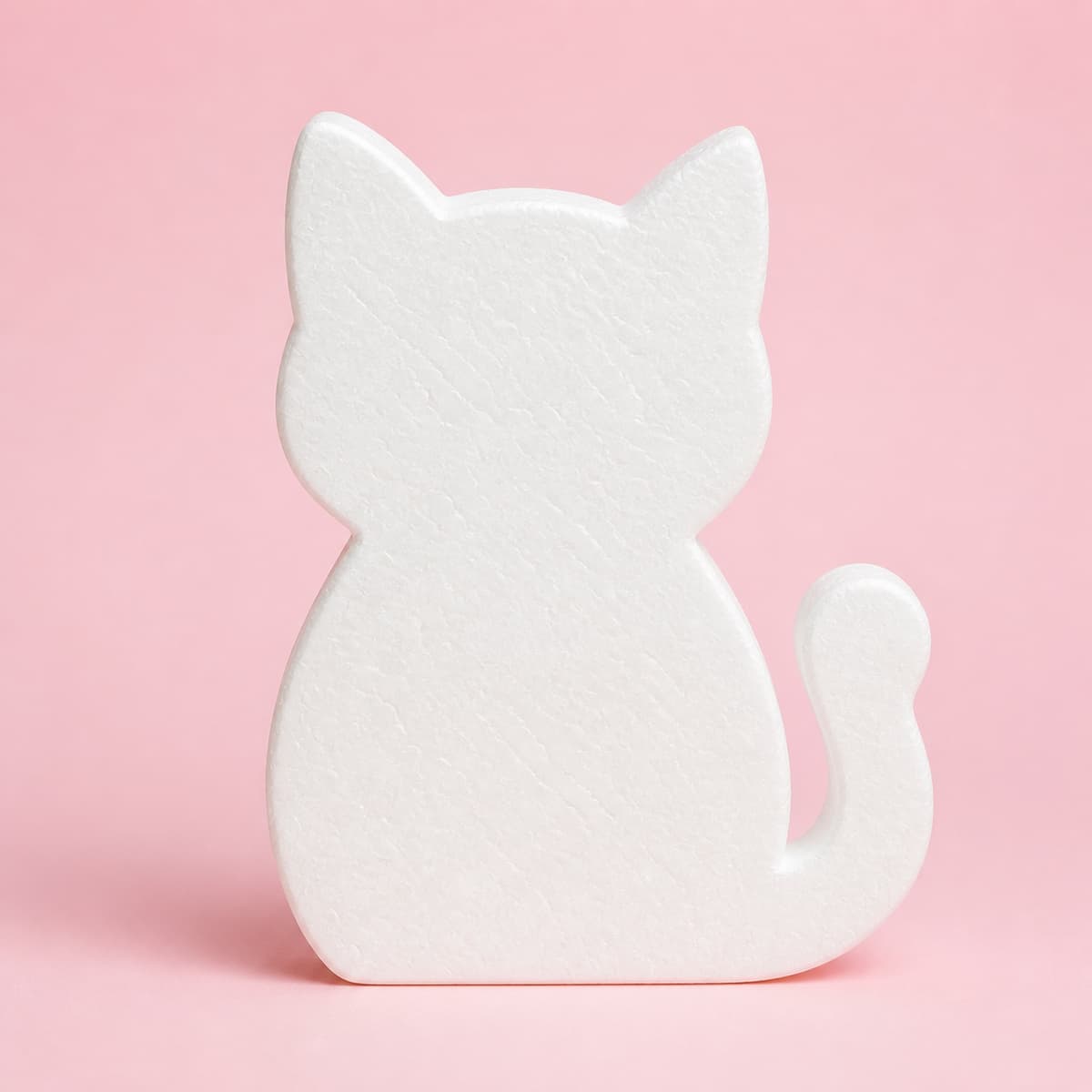 Silhouette de chat découpée dans une plaque de polystyrène blanc, posée de face sur fond pastel uniforme, avec un contour net et une épaisseur visible.