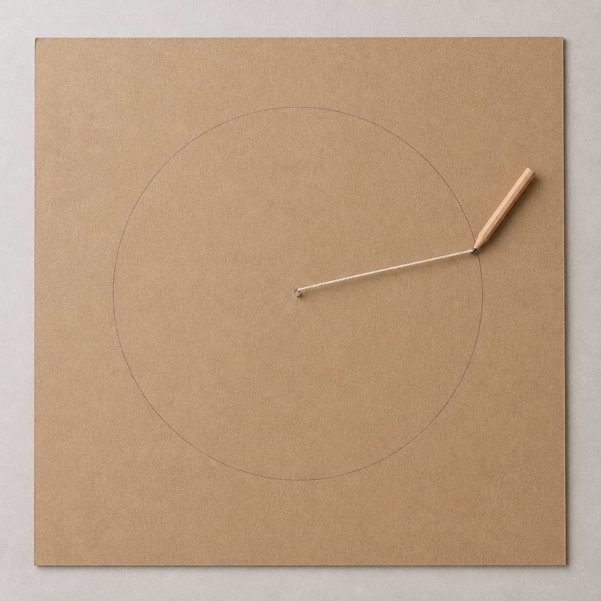 Vue de dessus d’une plaque de carton montrant un point central, un rayon tracé, un cercle au crayon et une ficelle reliée à un crayon, avec une marge périphérique.