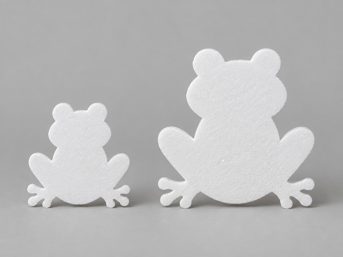 Deux silhouettes de grenouille en polystyrène blanc, une petite et une grande, posées côte à côte sur un fond neutre, avec des pattes découpées.