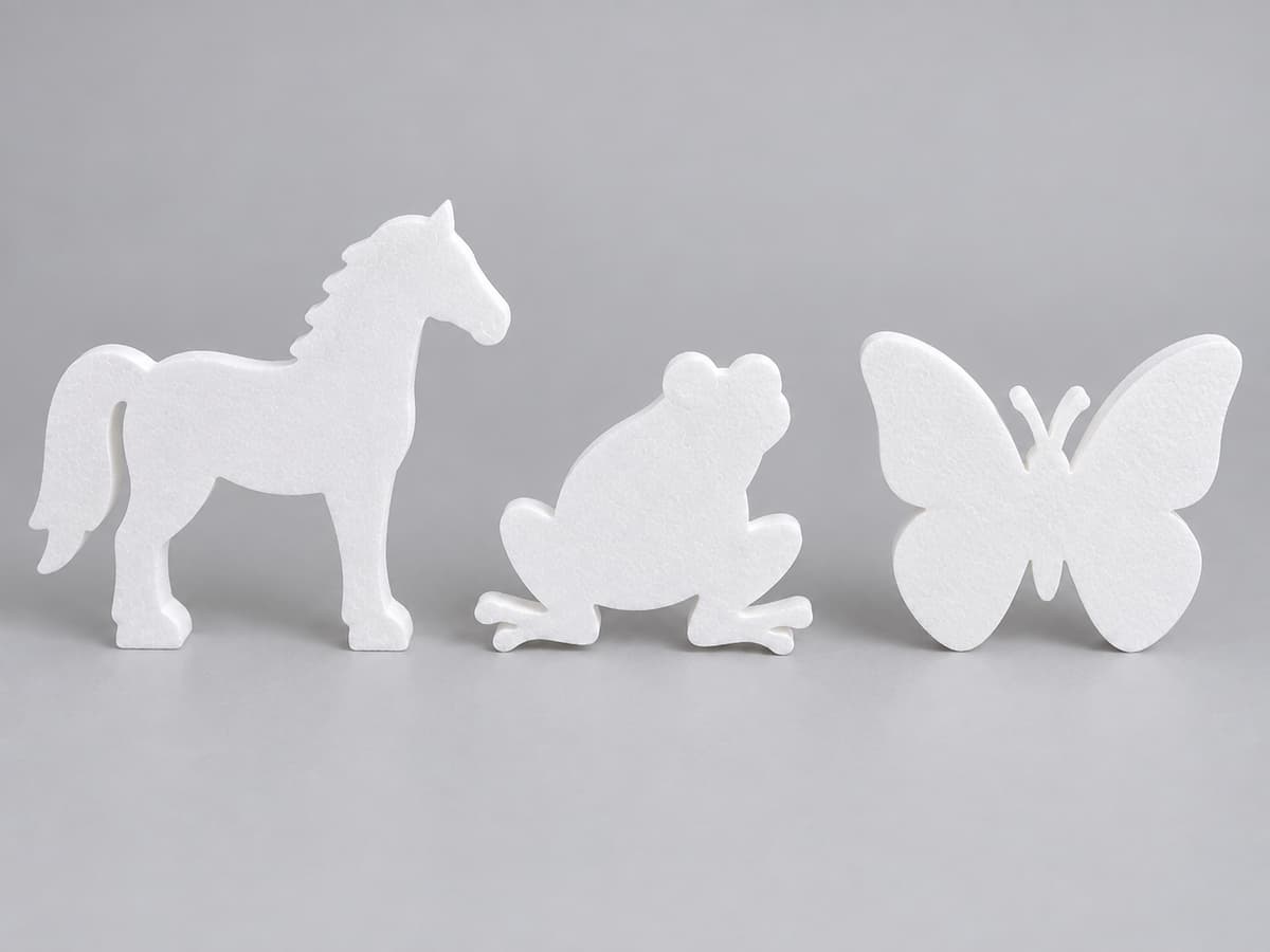 Trois silhouettes animales en polystyrène blanc représentant un cheval, une grenouille et un papillon alignées sur fond neutre.