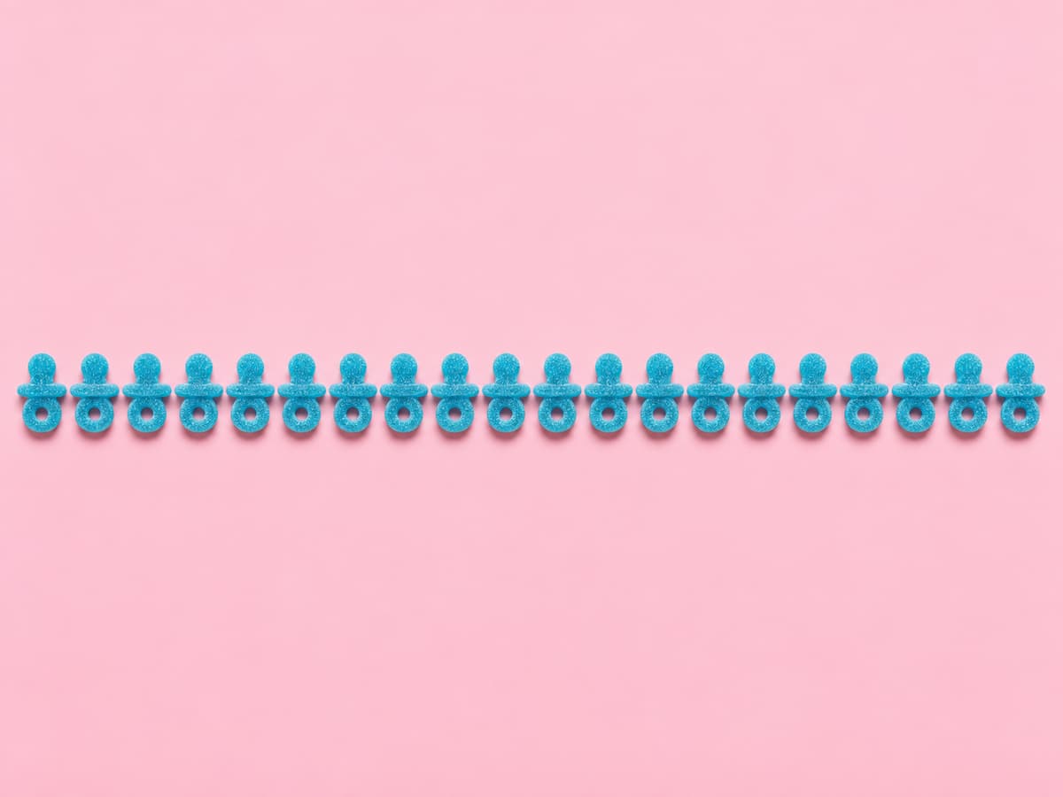 Vingt bonbons bleus en forme de tétine alignés sur un fond pastel uni.